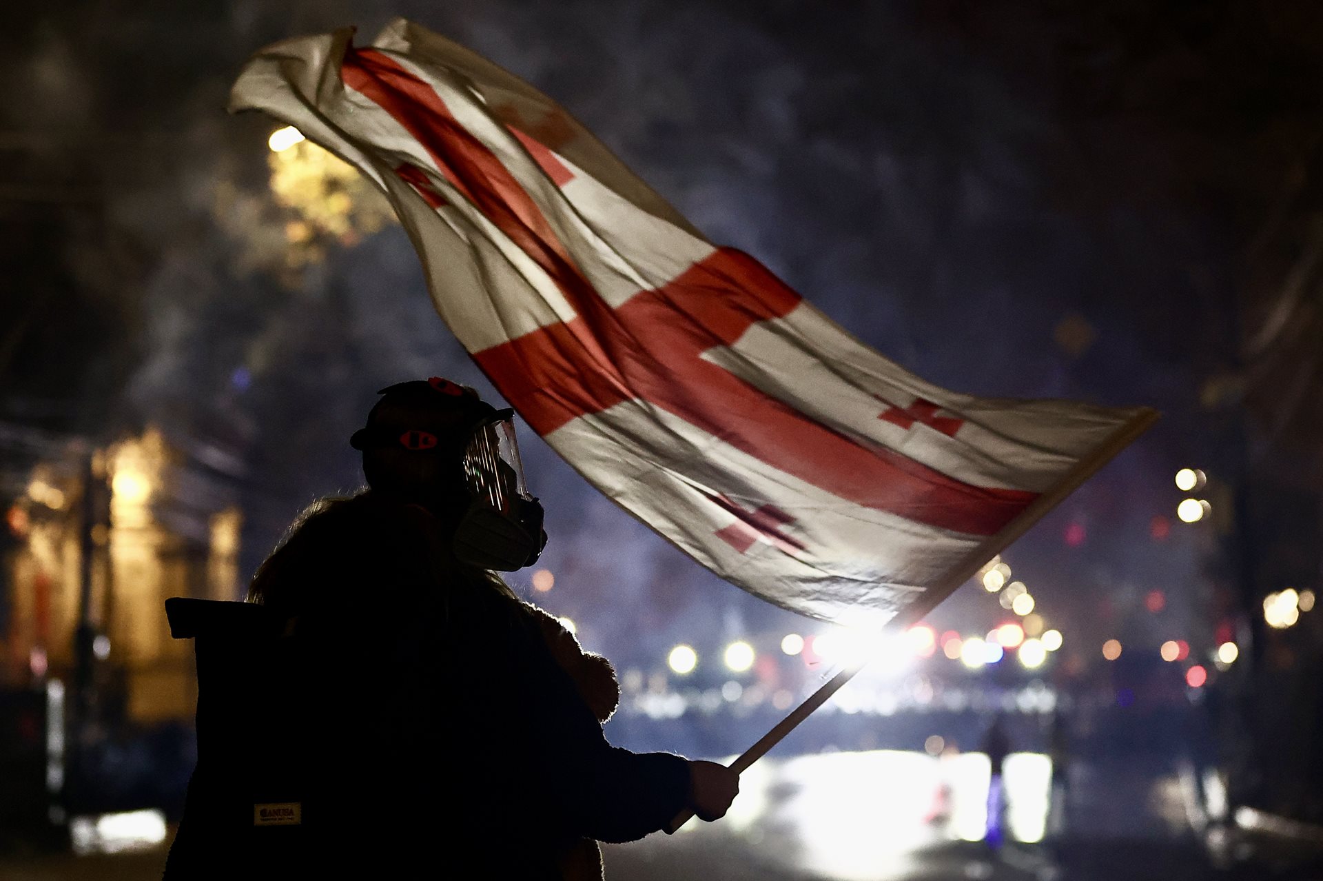 A protester wearing a giant teddy bear on their front waves a Georgian flag during an anti-government rally outside the Parliament of Georgia, in Tbilisi. Police (seen in a line in the background) were using tear gas against demonstrators.